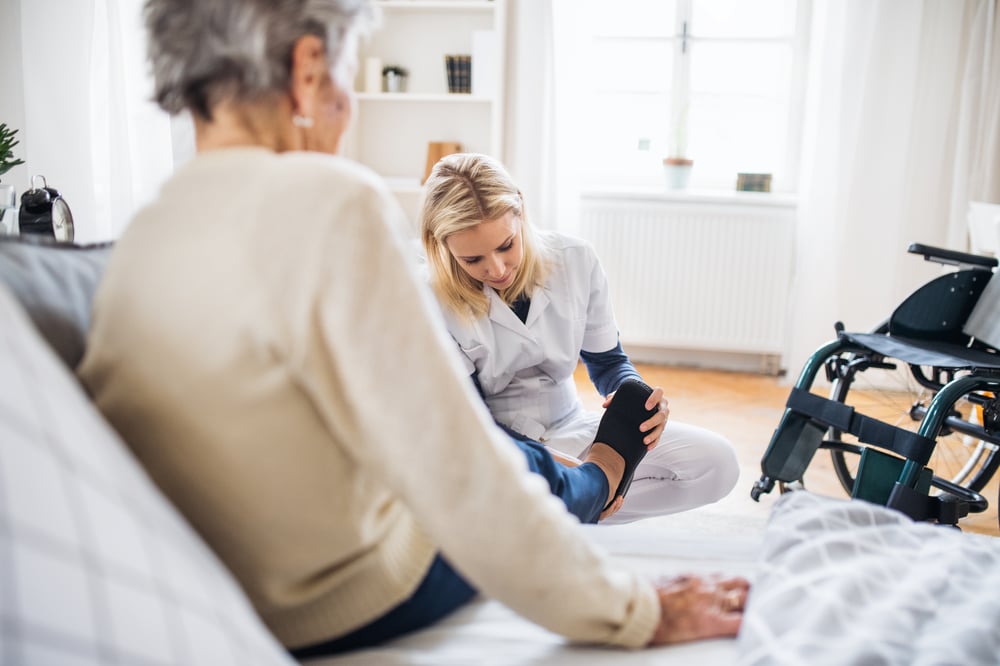health-visitor-putting-slippers-senior-woman-home