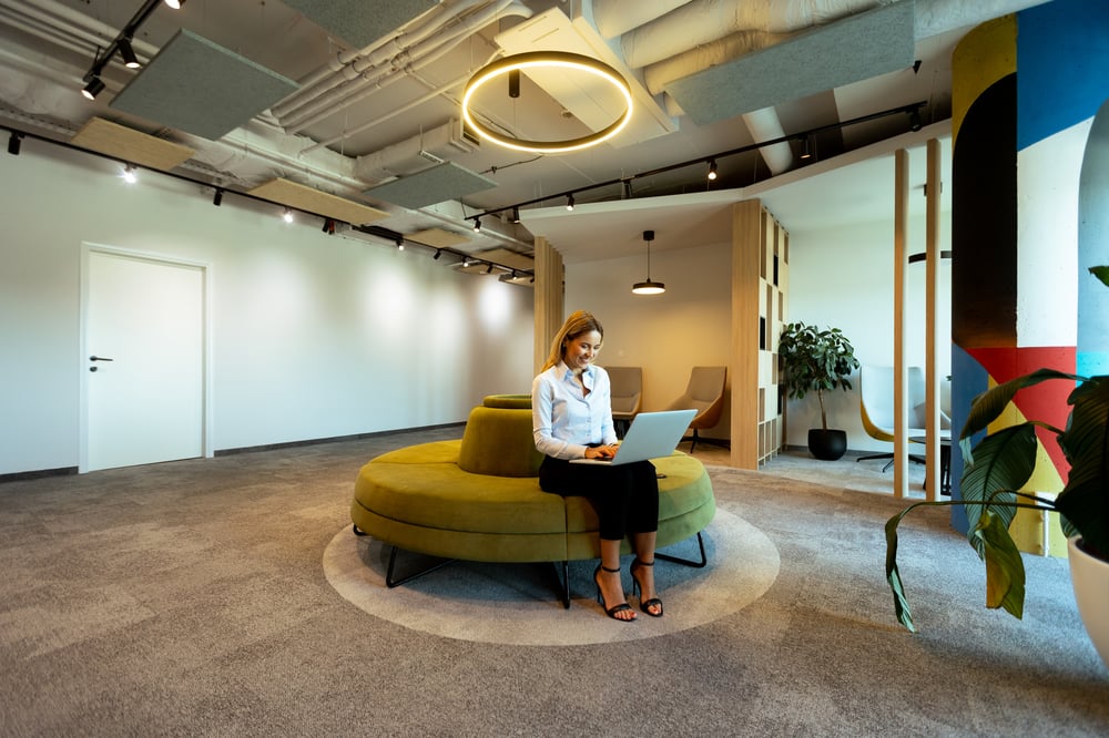 modern-office-lounge-with-green-circular-seating-woman-working-laptop-daytime