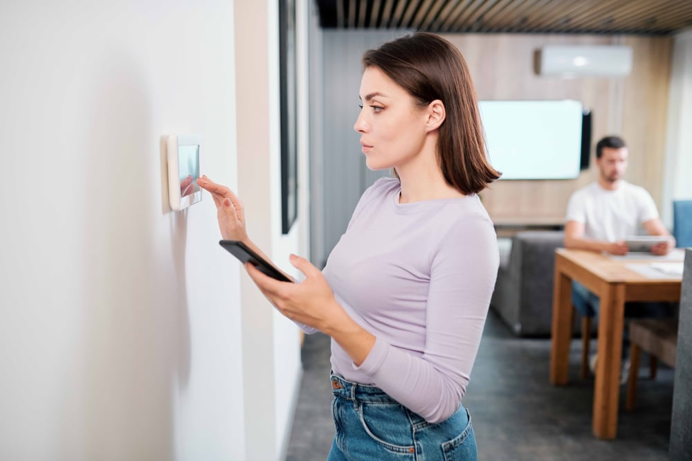 pretty-young-woman-with-smartphone-loading-smart-remote-control-application-touchpad-wall