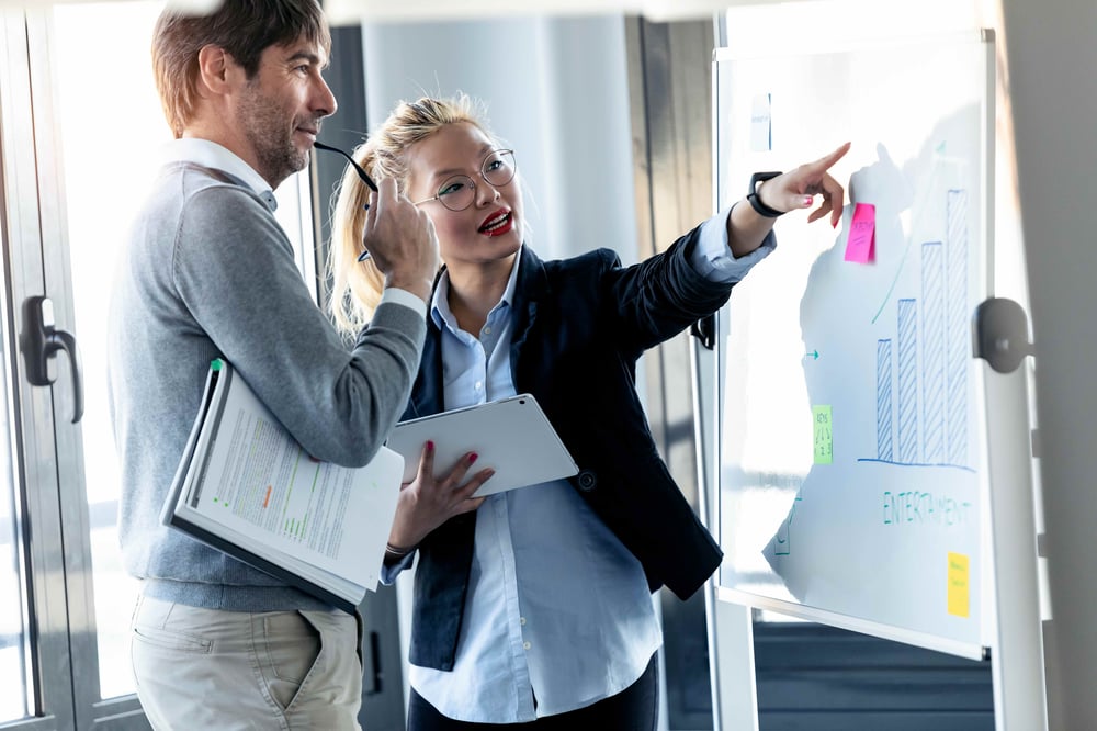 shot-elegant-young-businesswoman-pointing-whiteboard-explaining-project-her-colleague-coworking-place
