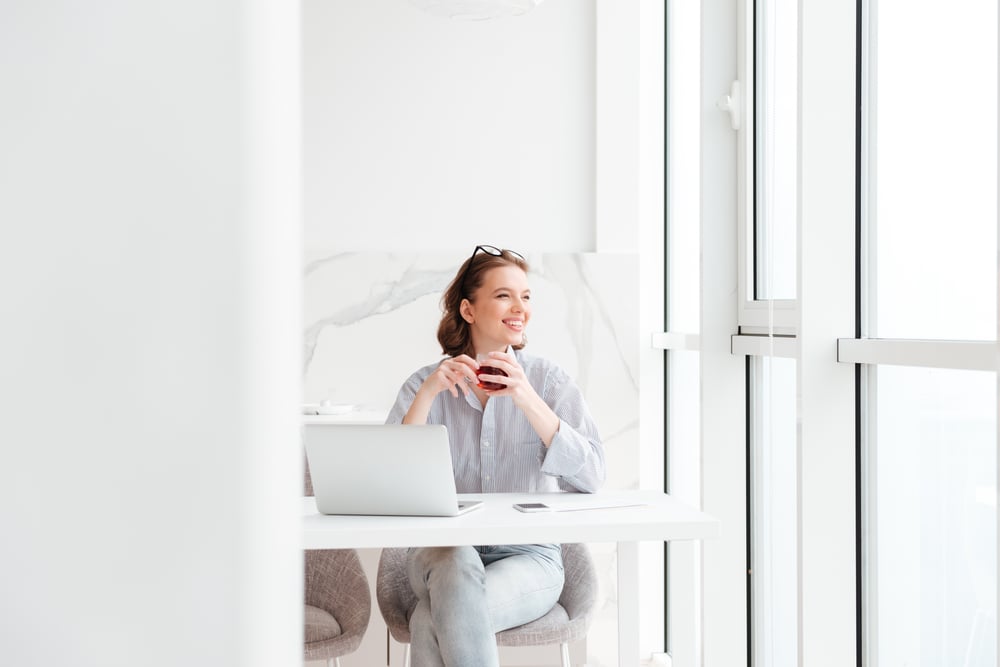 young-brunette-woman-holding-cup-tea-while-sitting-kitchen-looking-large-window